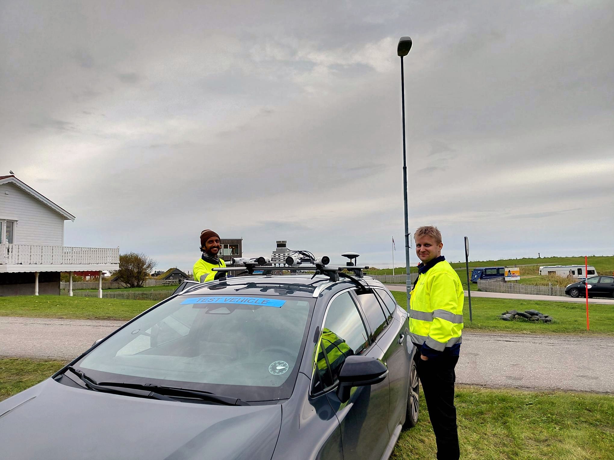 Two people, Safi and Matias standing next to the test vehicle that has an antenna and lidar camera on the roof